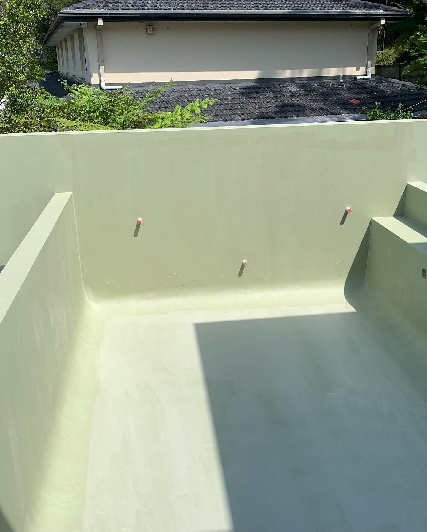 A Large White Swimming Pool With A House In The Background — Coastwide Waterproofing in Hornsby, NSW