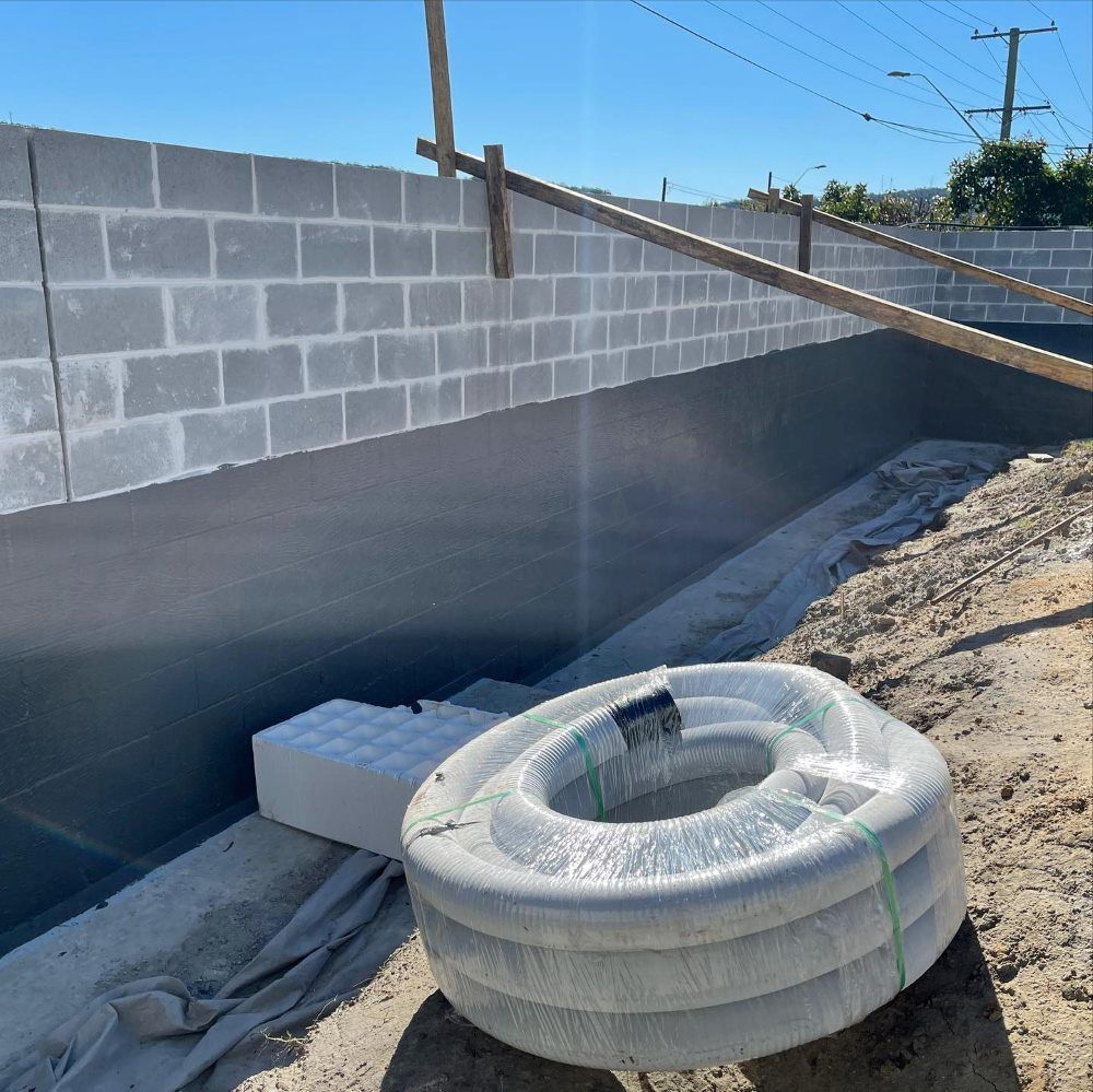 A Large Hose Is Sitting In The Dirt In Front Of A Brick Wall — Coastwide Waterproofing in Terrigal, NSW