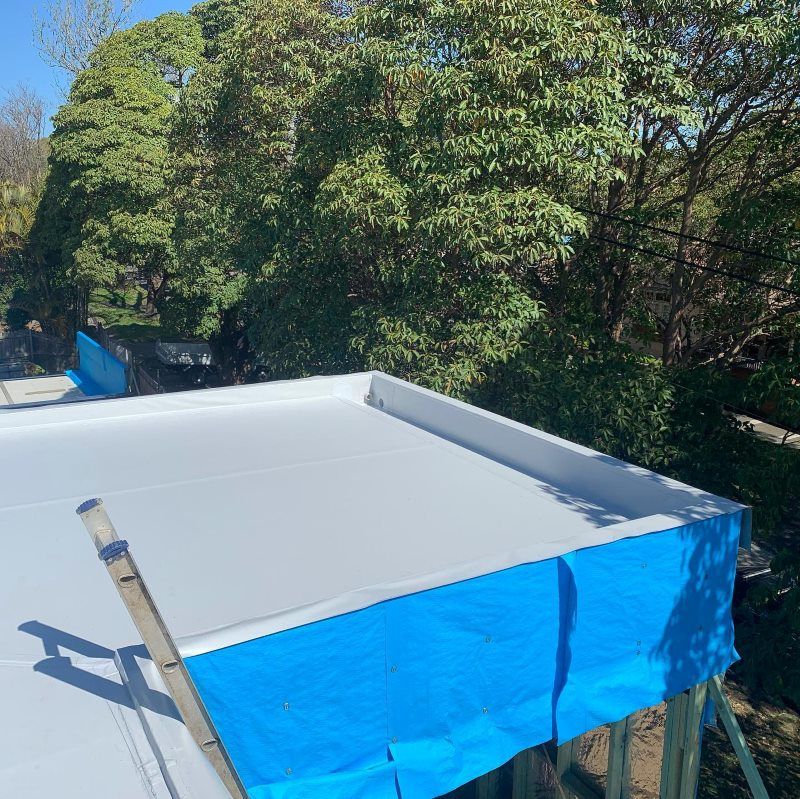 A Roof With A Blue Tarp On It And Trees In The Background — Coastwide Waterproofing in West Gosford, NSW
