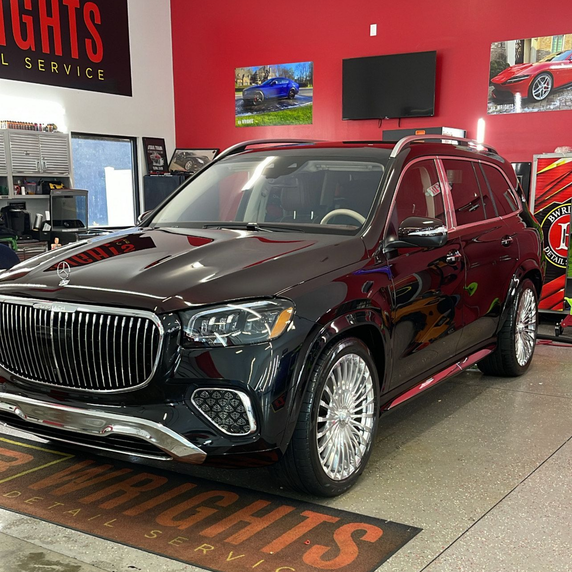 Black SUV with chrome rims parked in a shop with red walls, logo visible.