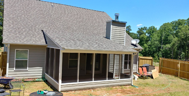 Backyard house with screened porch, large roof, and fenced yard on a sunny day