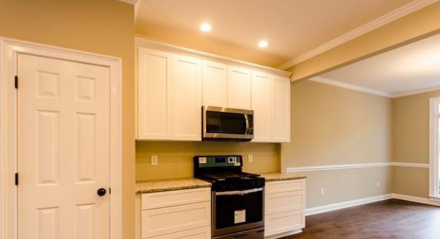 Bright empty kitchen with white cabinets, black stove, and a microwave in a beige room with hardwood floors