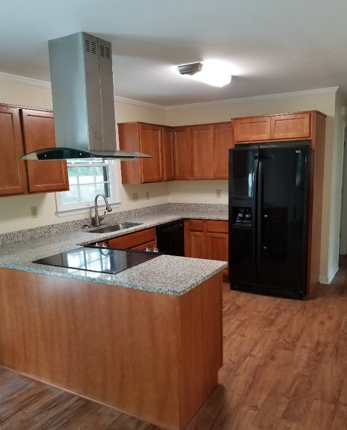 Modern kitchen with wood cabinets, granite island, black refrigerator, and stainless steel range hood.