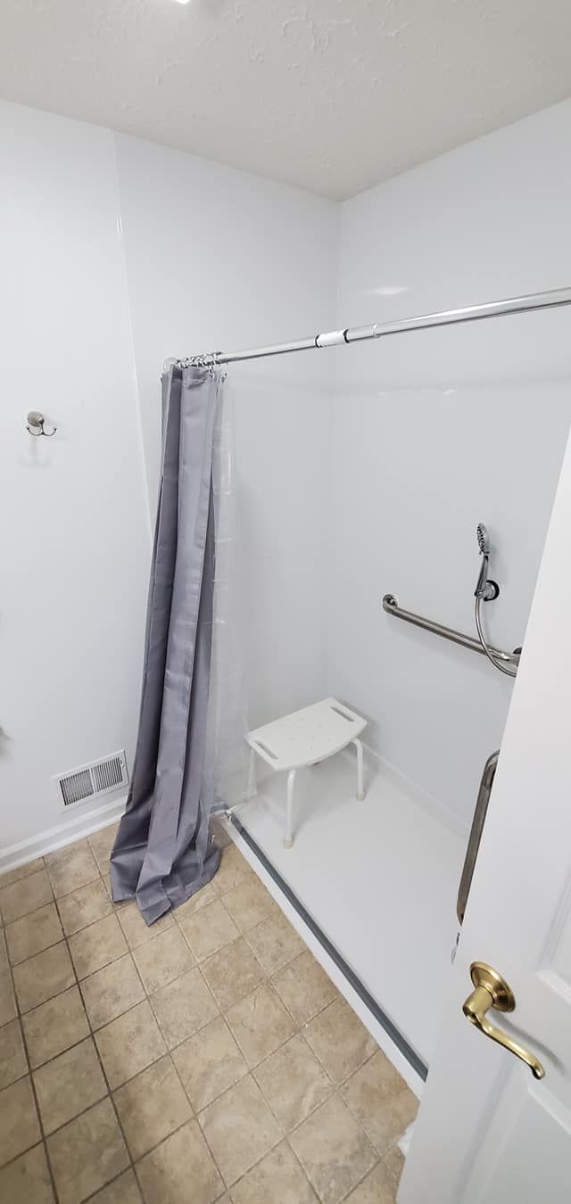 A bathroom with a walk in shower and a stool.