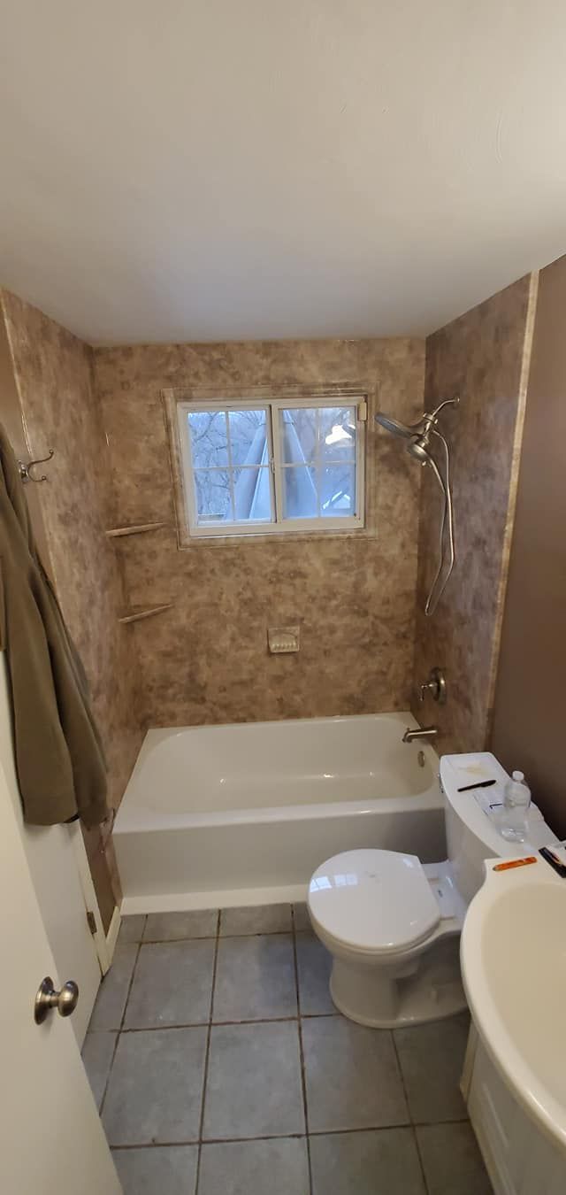 A bathroom with a tub , toilet , sink and window.