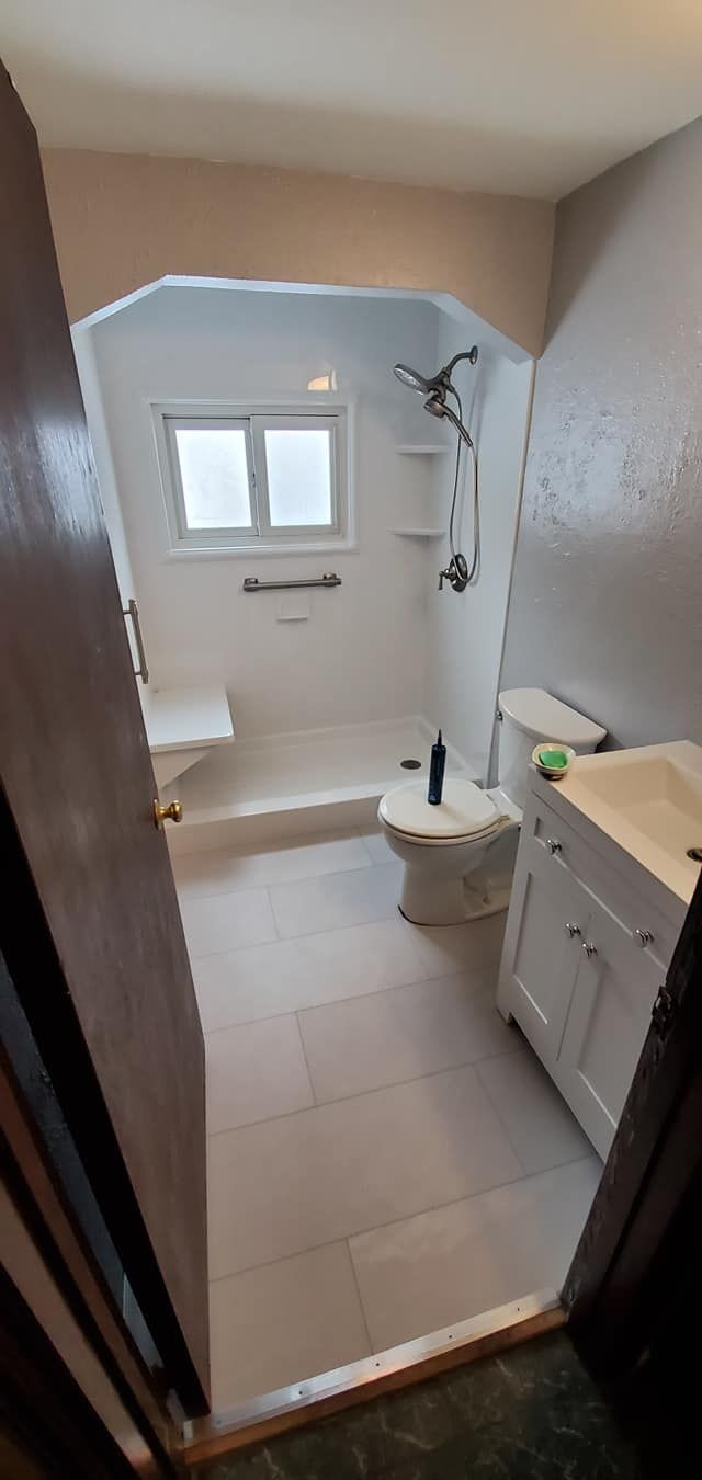 A bathroom with a toilet , sink , shower and window.