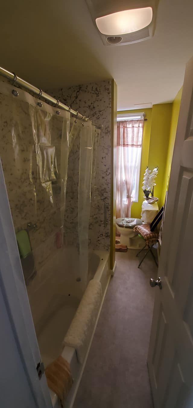 A bathroom with a tub , shower , toilet and window.
