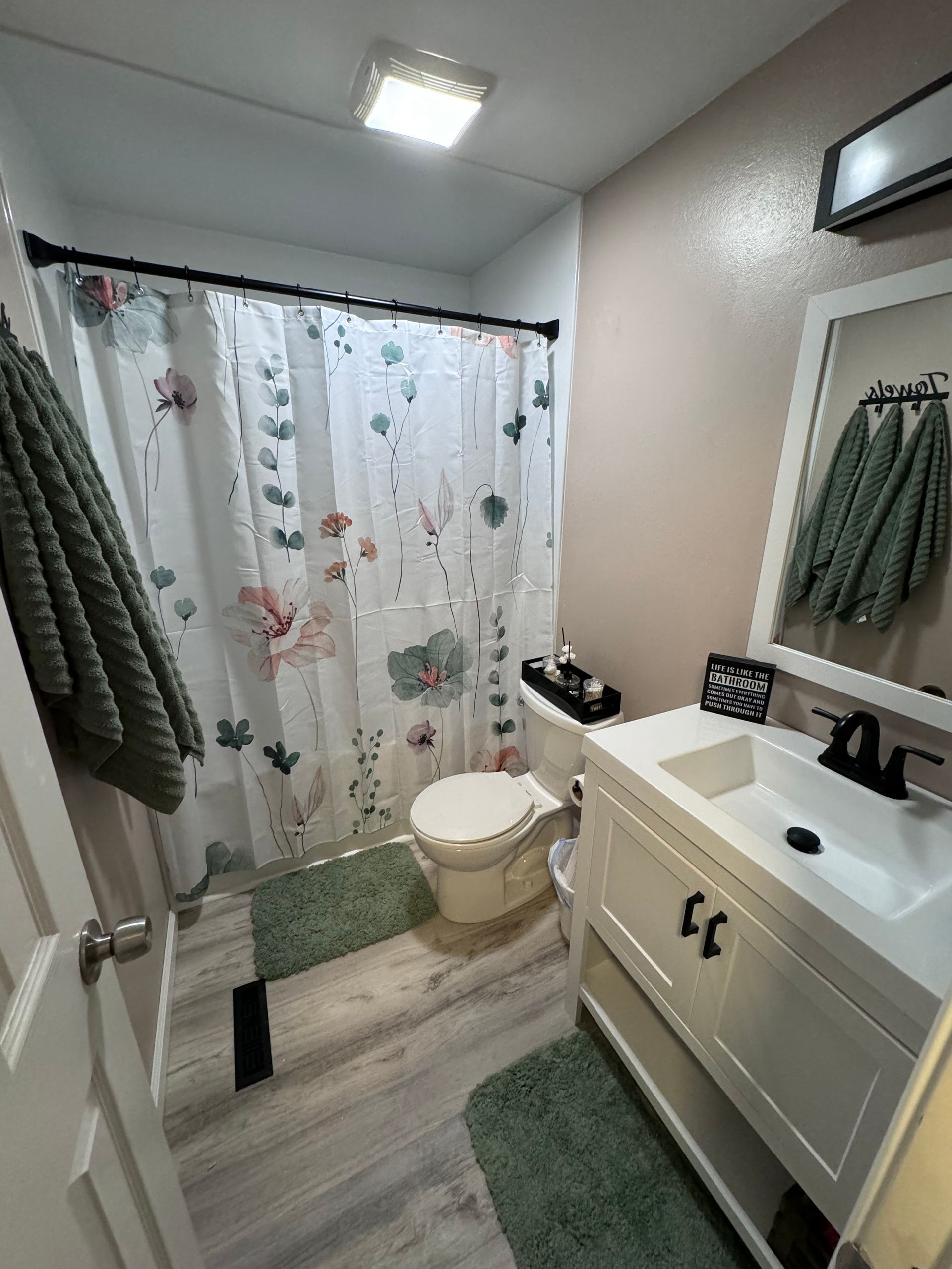 A bathroom with a toilet , sink , mirror and shower curtain.