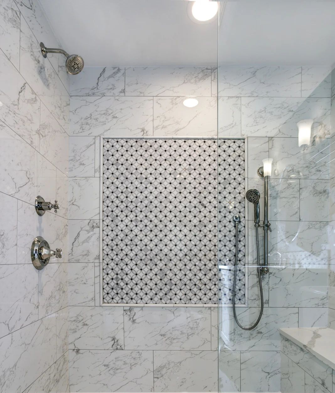 White tiled shower with bathtub, mosaic niche, and handheld showerhead.