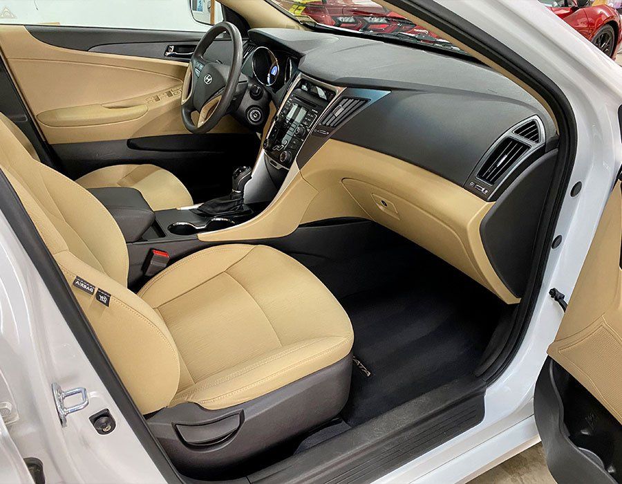 Tan leather car interior with black dashboard, open passenger door, and front seats visible