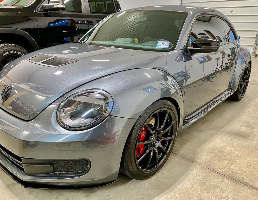Silver Volkswagen Beetle coupe with black rims and red brake calipers parked indoors.