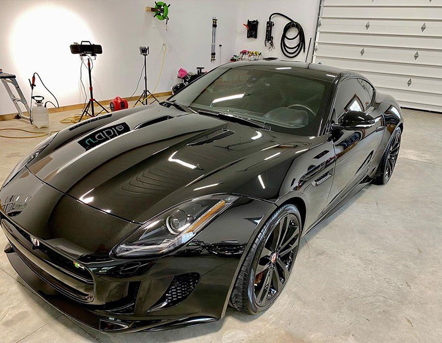 Black sports car in a garage, viewed from the front-left with glossy reflective paint.