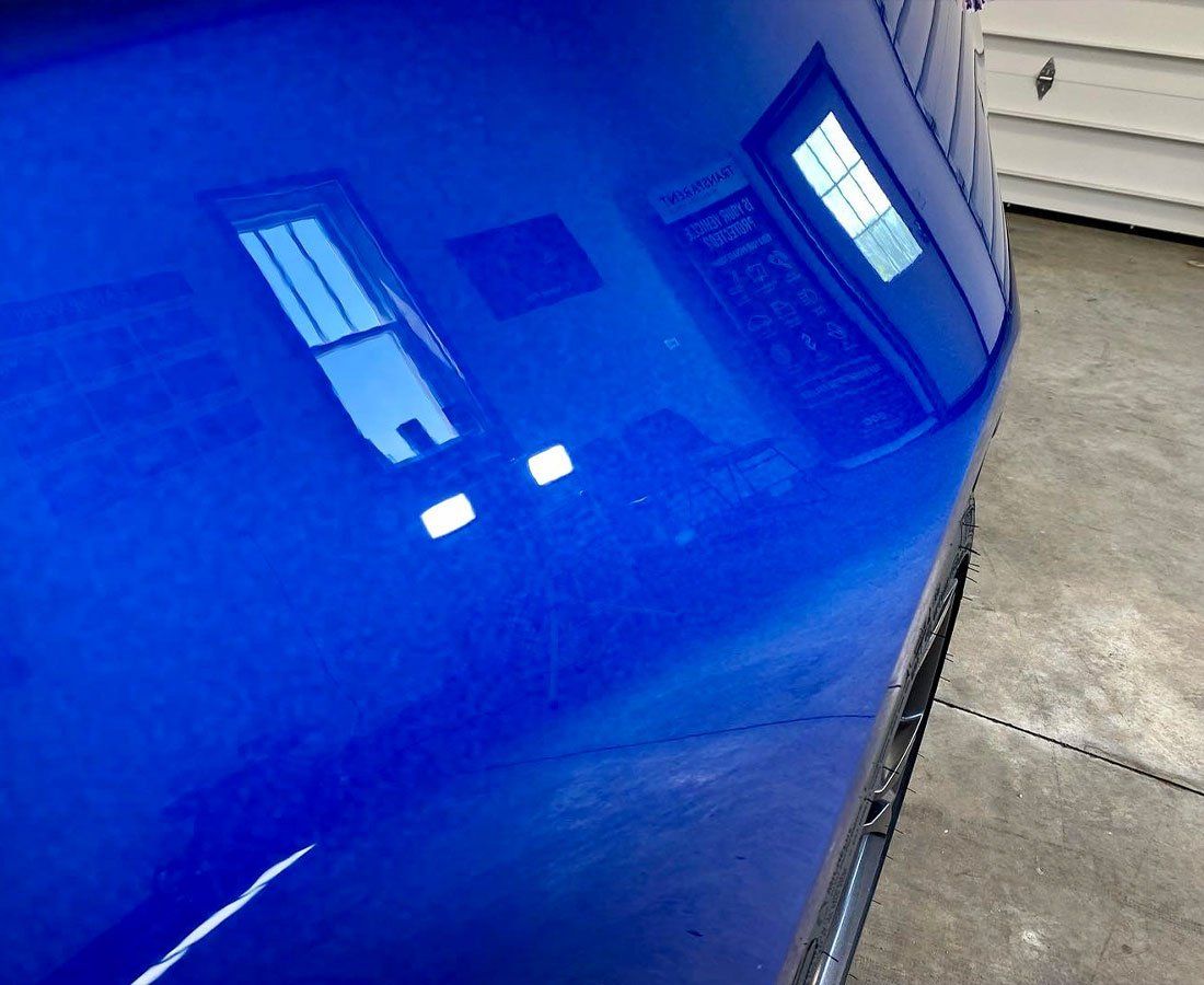 Close-up of a blue car hood reflecting a house and garage windows.