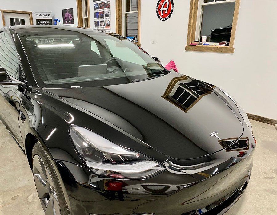 Black sports car in a garage, showing a glossy hood and windshield reflection.