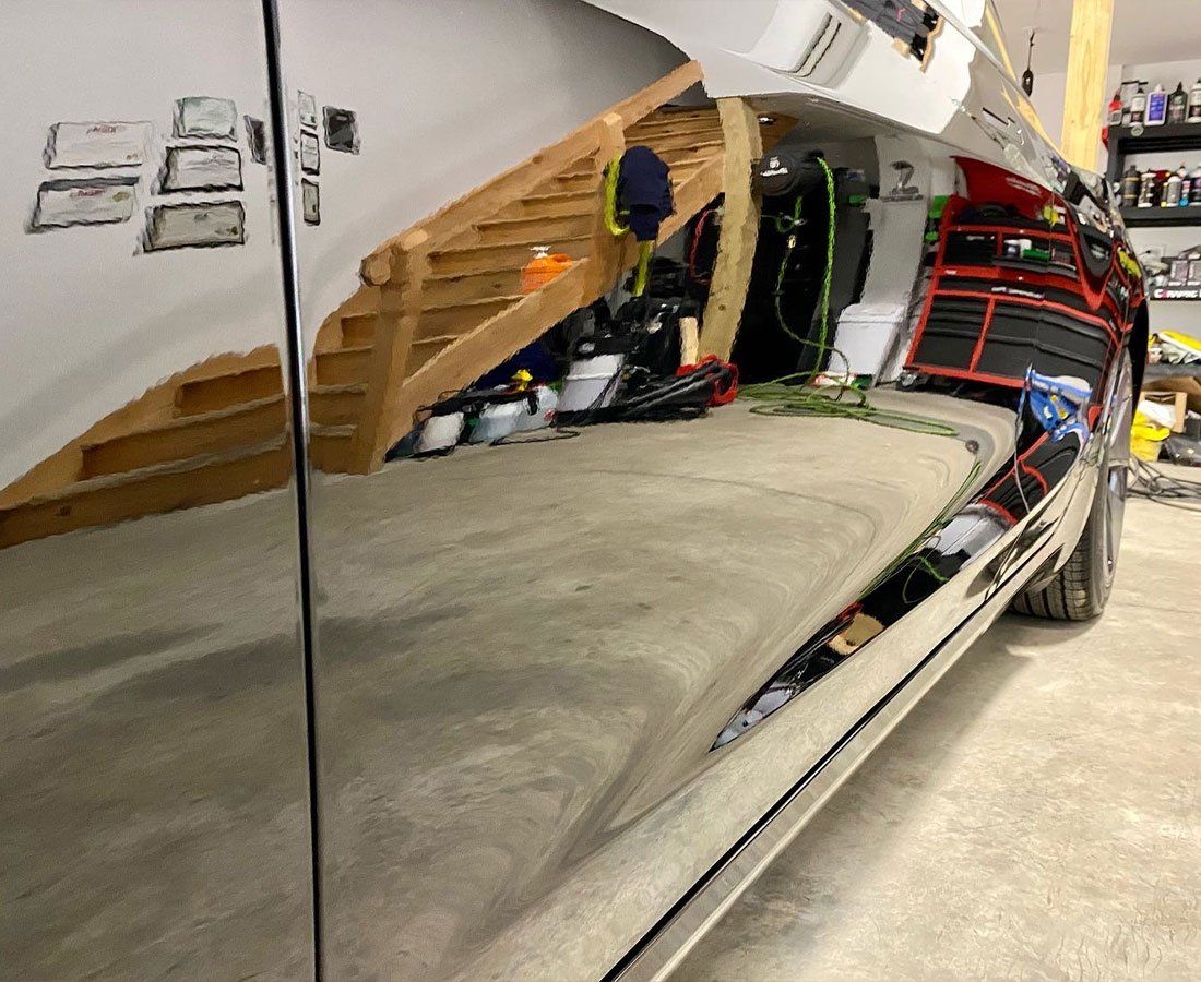 Shiny black vehicle side panel reflecting a garage interior with stairs and tools