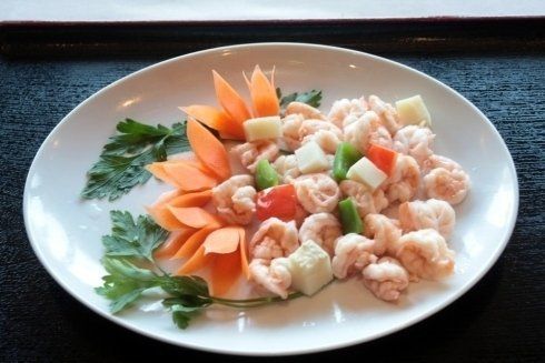 Insalata di gamberi impiattata con guarnizione di fiore di carota e foglie di prezzemolo su un piatto bianco.