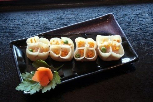 Rotoli di sushi su un piatto nero con guarnizione di zenzero marinato e verdure.