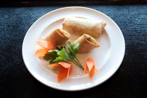 Piatto bianco con involtini primavera, guarnizione di carote e prezzemolo su un tavolo scuro