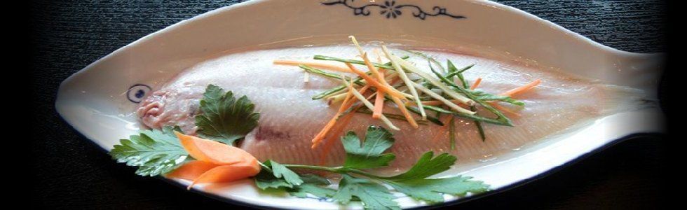 Pesce intero guarnito con erbe aromatiche e carote grattugiate su un piatto bianco.