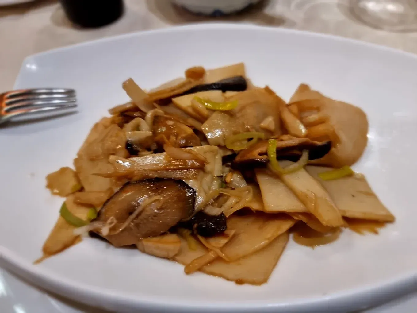 Piatto di spaghetti di riso saltati in padella con funghi e verdure, servito su un piatto bianco.