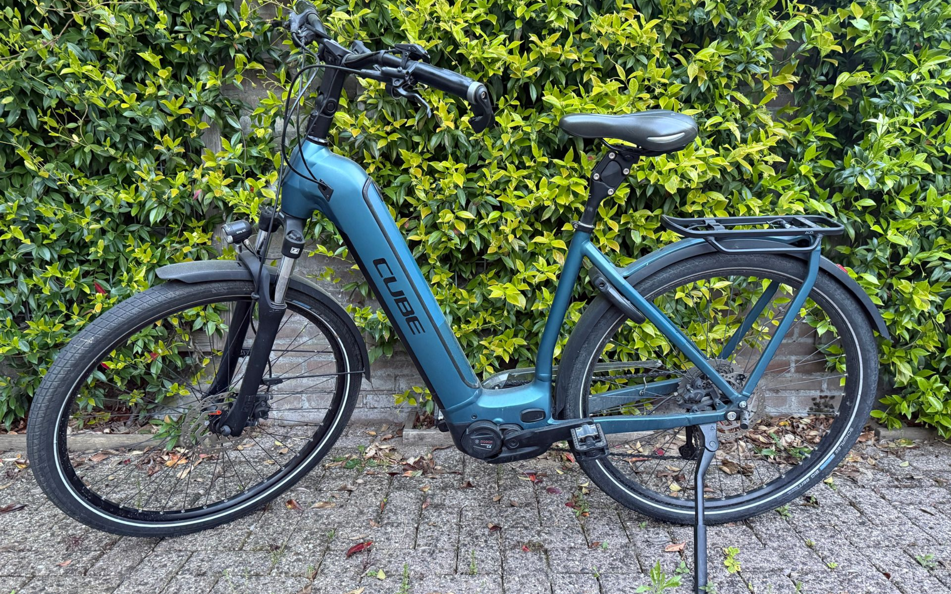 Grijze elektrische fiets met bagagedrager en spatborden, in zijaanzicht weergegeven op een witte achtergrond.