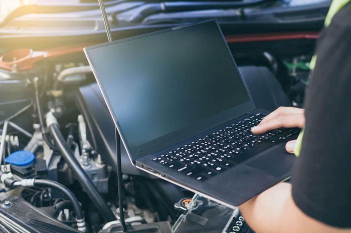 Una persona sta usando un computer portatile sotto il cofano di un'auto.
