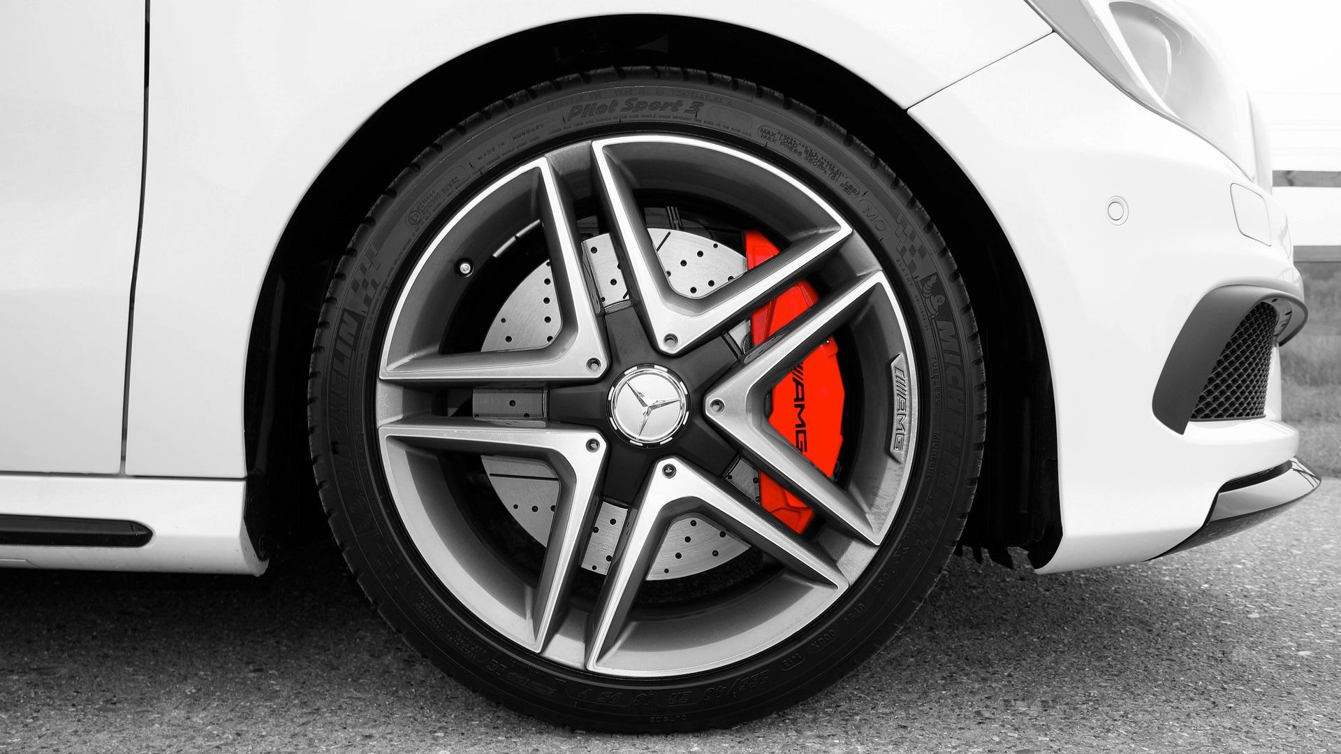 White car wheel with silver spokes, red brake calipers, and black tire.