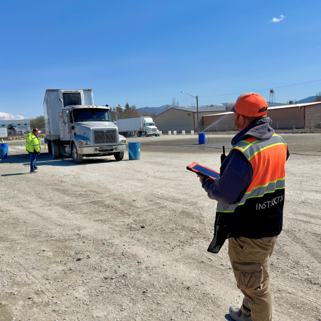 Worker in orange vest and hard hat directing a concrete mixer at a construction site under a blue sky