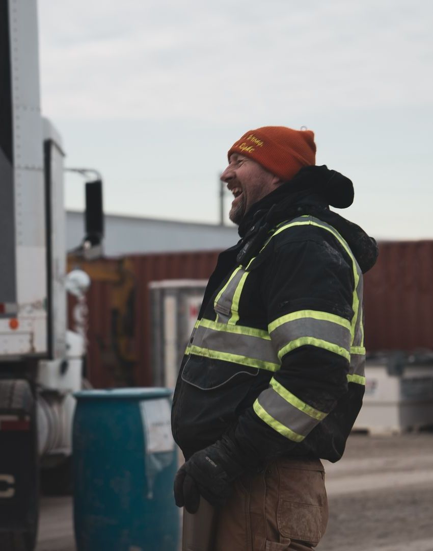 A CDL instructor wearing a beanie and safety vest is standing in front of a truck
