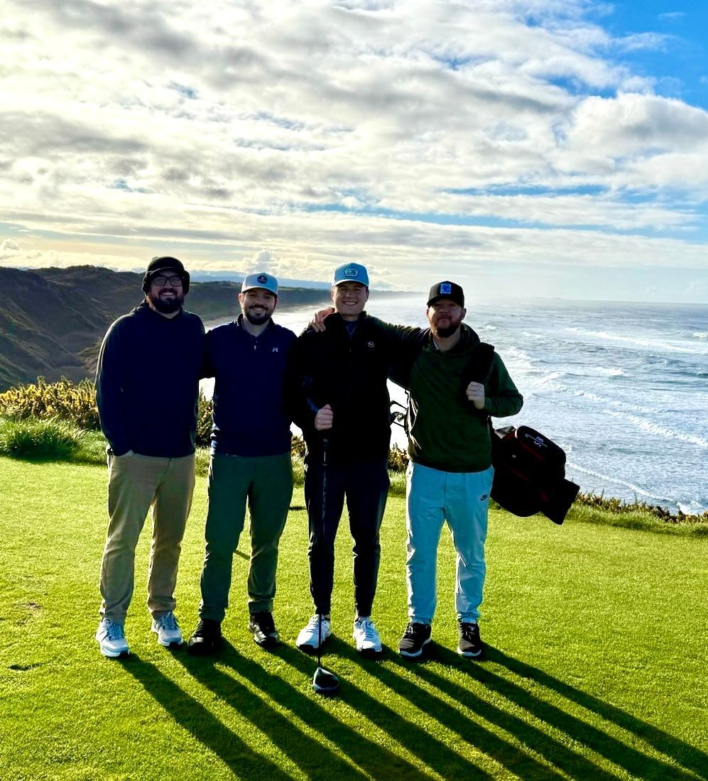 CDL PowerSuite team on a grassy cliff overlooking the ocean under a bright, cloudy sky.