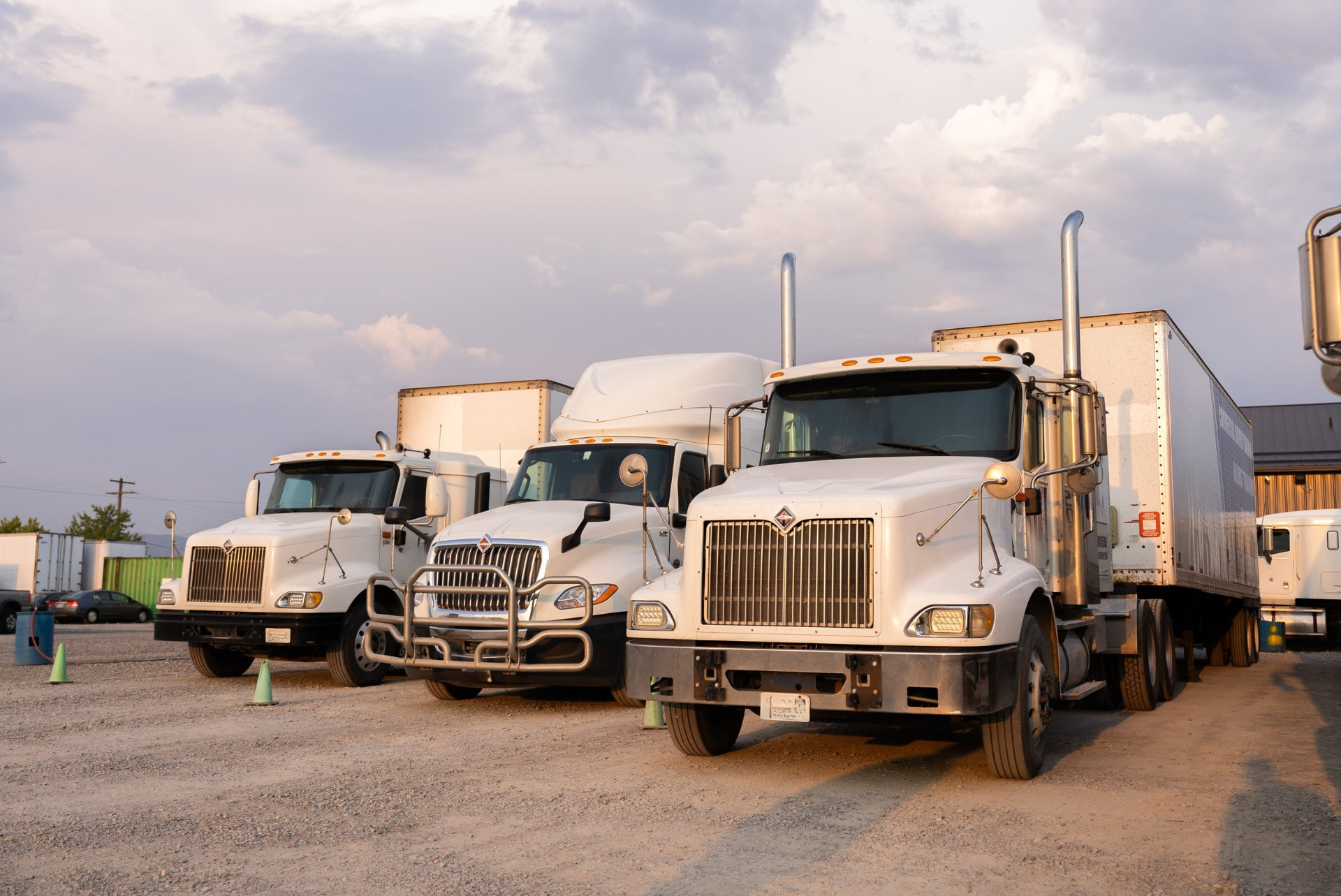 Row of white semi trucks lined up at a commercial truck driving school lot.