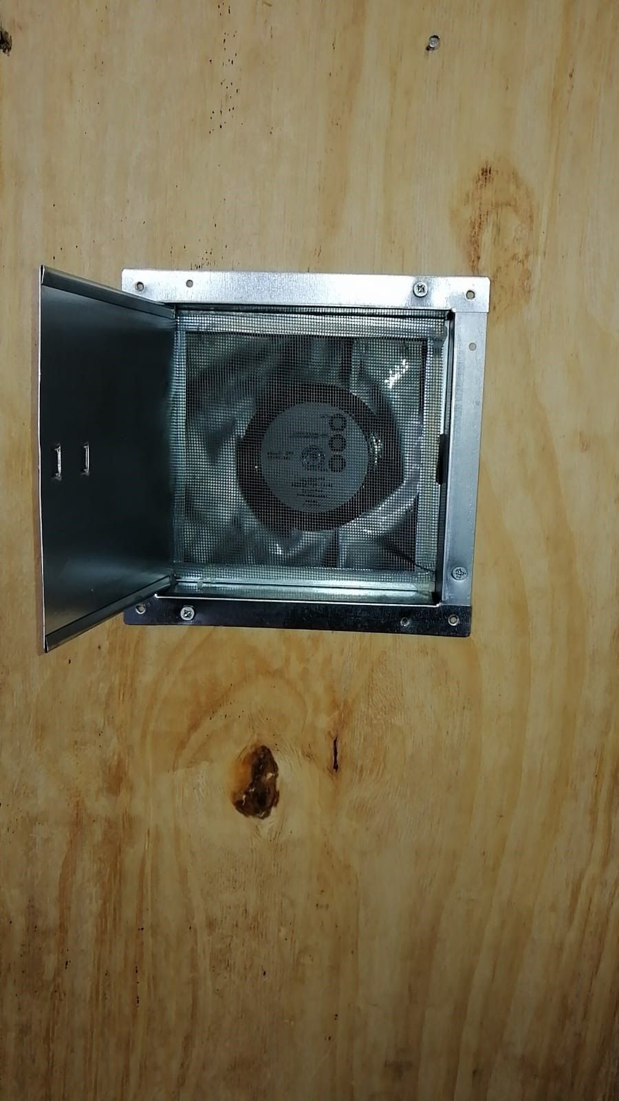 Griglia di ventilazione metallica aperta con ventola montata su un pannello di legno a muro