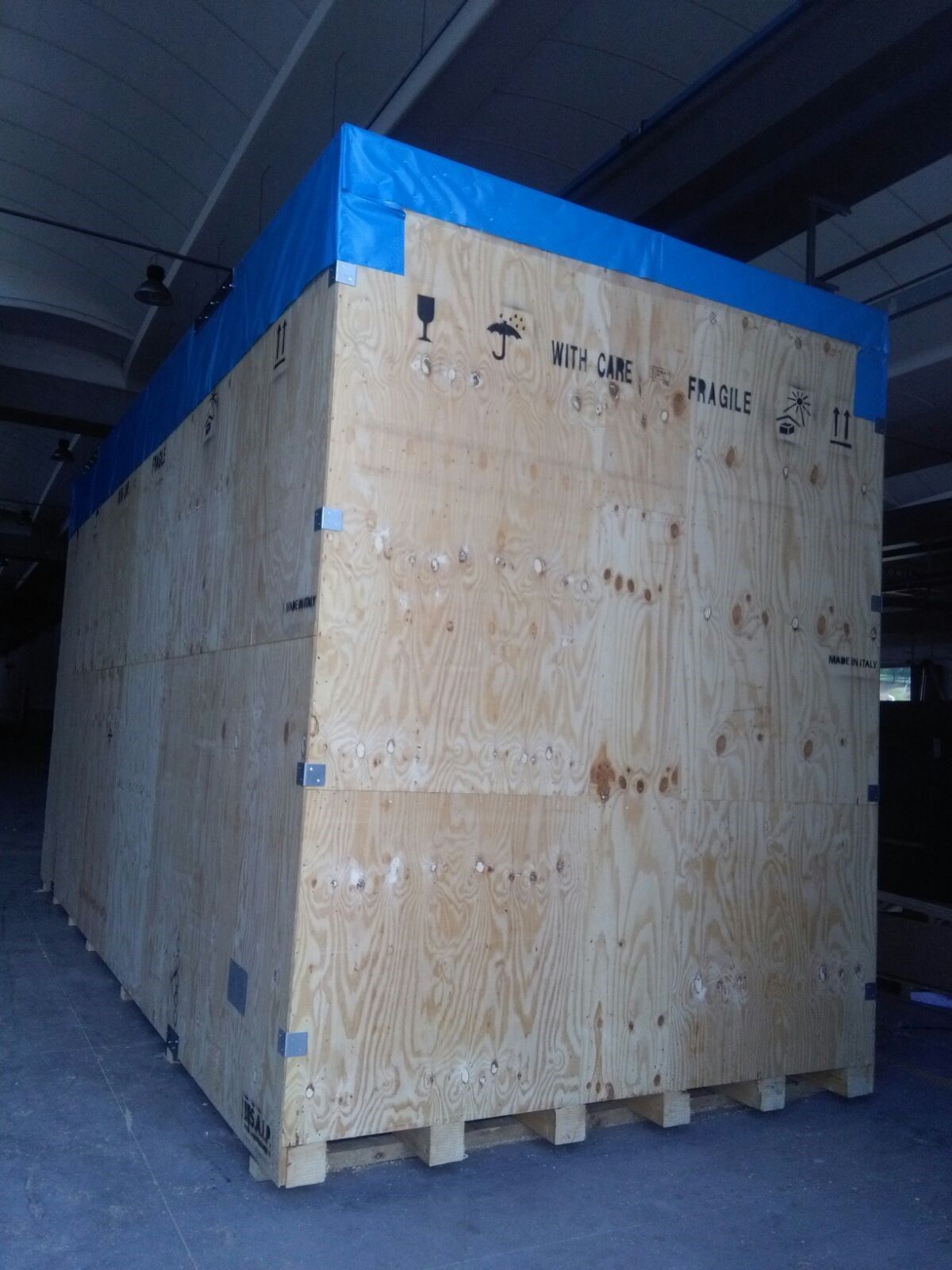 Grande cassa di legno per spedizioni con bordo superiore blu all'interno di un magazzino