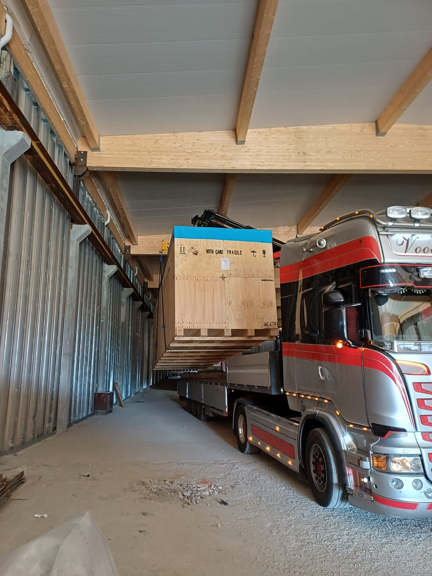 Un camion semirimorchio rosso trasporta una cassa di legno all'interno di un'area di carico di un magazzino.