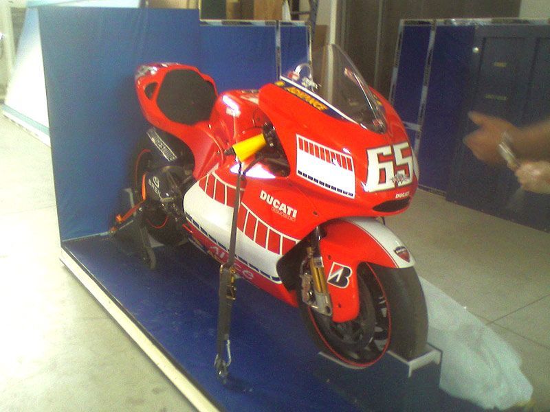 Motocicletta da corsa rossa su piedistallo con il numero 65 e il marchio Ducati.