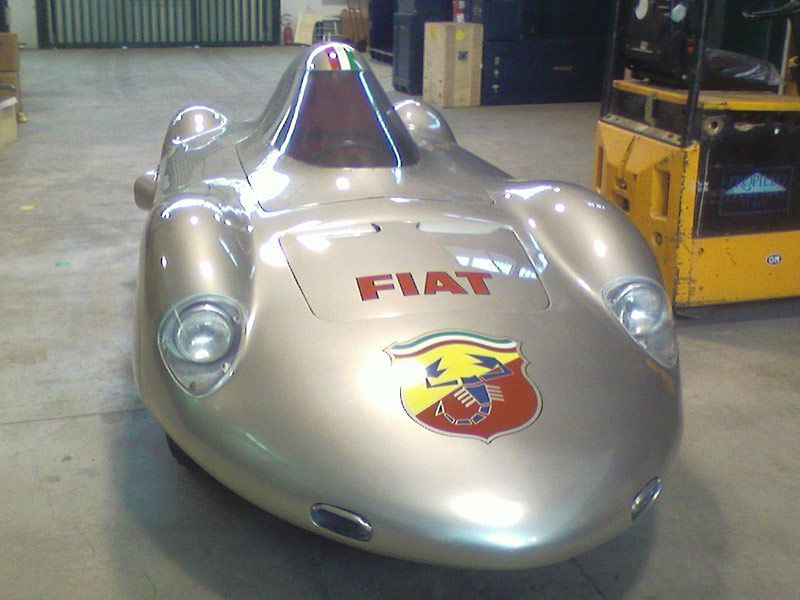 Fiat da corsa d'epoca color argento con logo rosso, mostrata in un garage.