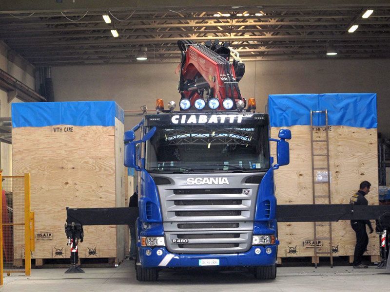 Camion Scania blu parcheggiato all'interno con grandi casse di legno su entrambi i lati e un carico rosso sopra.