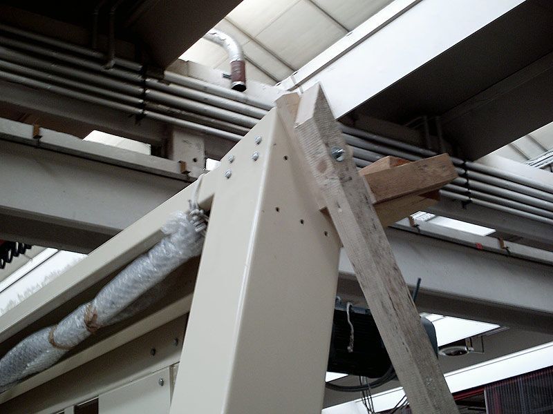 Struttura del tetto di un magazzino industriale con travi in ​​acciaio e tubazioni aeree sotto un soffitto metallico.