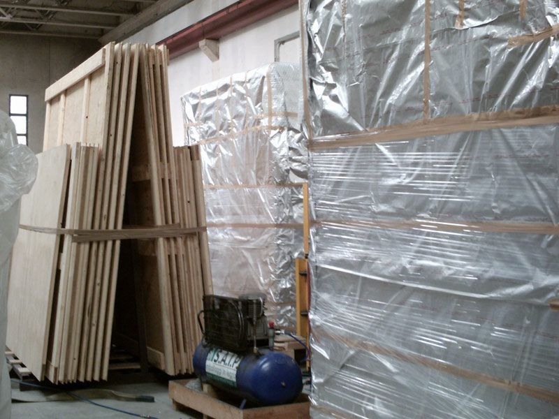 Tavole di legno impilate e materiali imballati, stoccati in un magazzino industriale.