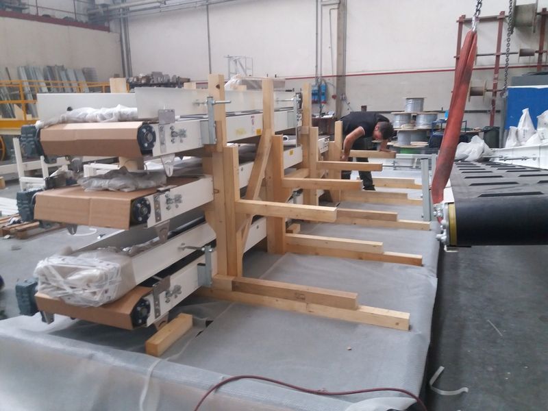 Magazzino con scaffali di legno impilati, attrezzature imballate e una scala rossa lungo la parete.