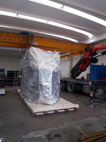 Pallet imballato su un carrello in un magazzino, con un camion gru accanto.