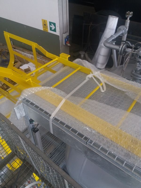 Macchinari industriali gialli con griglie e tubi metallici all'interno di un ambiente di fabbrica