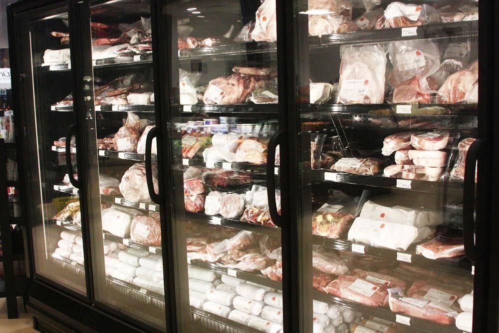 A meat display case with glass doors filled with various packaged cuts of meat on shelves.