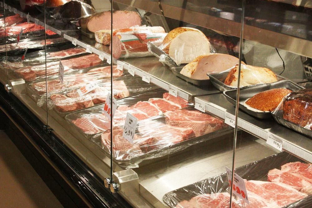 A butcher's display case filled with various cuts of raw meat and deli products on trays.