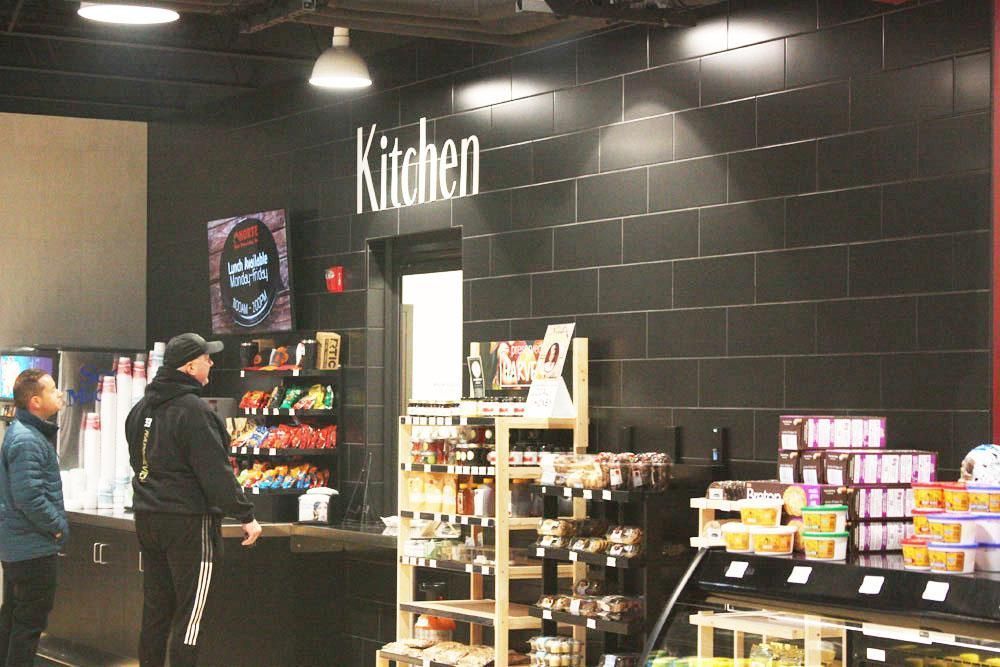 A person in a black hoodie stands at a counter labeled