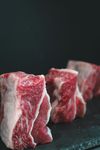 Three thick, raw cuts of marbled red beef standing upright on a dark, textured stone surface against a black background.