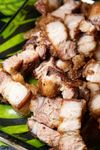 A pile of crispy, golden-brown chopped pork belly pieces served on a dark patterned plate.