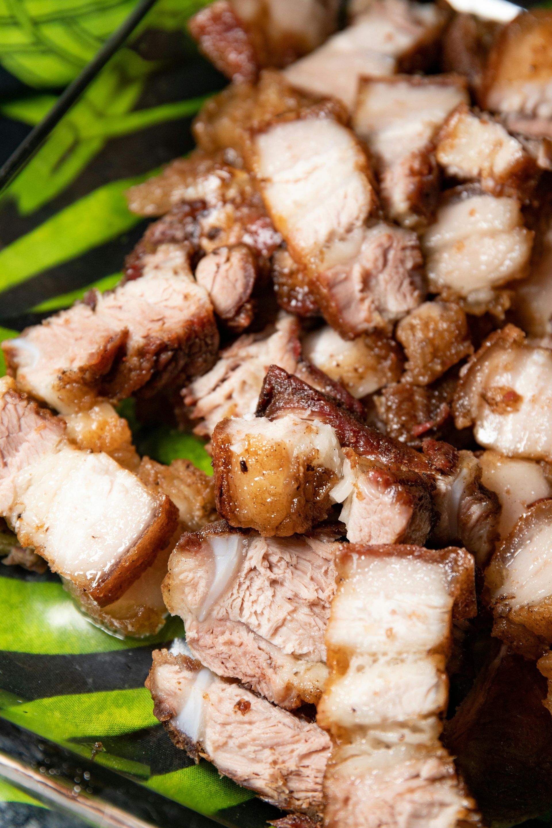 A pile of crispy, golden-brown chopped pork belly pieces served on a dark patterned plate.