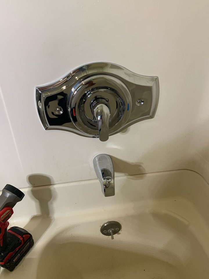 Bathtub faucet and knobs above a white tub, with a red power drill on the left side.