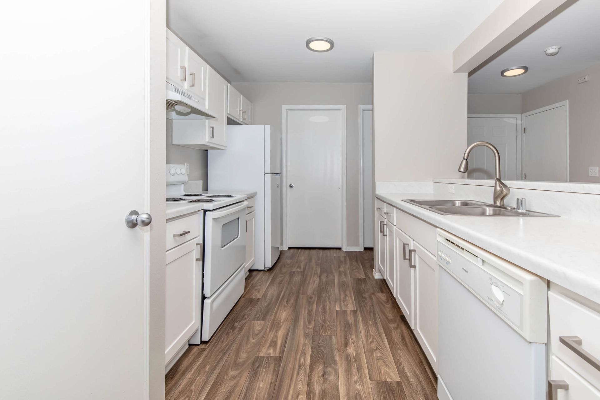 A kitchen with white cabinets , white appliances , a sink and a refrigerator.